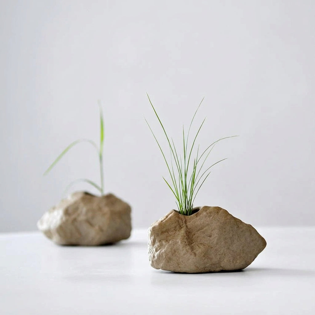 Two stone-like planters with grass growing out of them on a white background