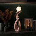 Decorative pink lamp on a shelf with a vase of flowers and books in the background.