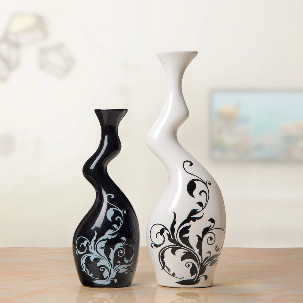 Two decorative wavy ceramic vases on a tabletop, one glossy black with a light blue floral scroll pattern and one glossy white with a black floral scroll pattern. A text overlay in the top right shows dimensions: large 32cm high by 9cm wide, small 24cm high by 8cm wide.