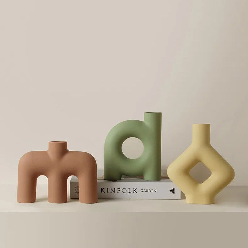 Three ceramic vases in brown, green, and yellow on a beige surface with a neutral background.