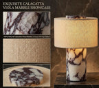A marble table lamp with a textured beige fabric drum shade and a cylindrical base carved from natural calacatta viola marble, shown beside three detail inset images highlighting the marble veining and the woven shade texture. Text reads 'EXQUISITE CALACATTA VIOLA MARBLE SHOWCASE' and 'Each piece is one-of-a-kind.