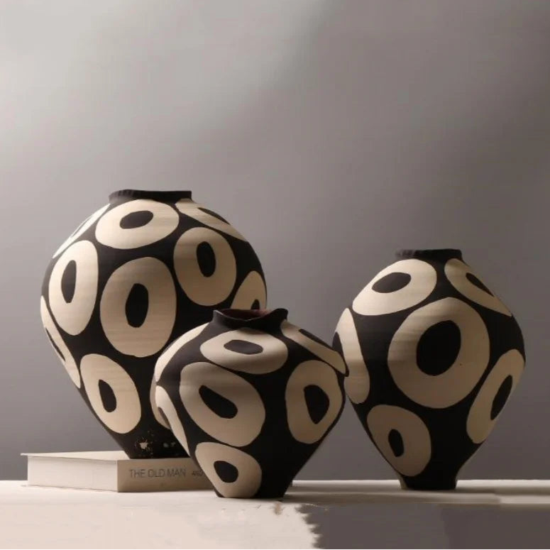 Three black and white patterned vases on a gray surface with a gray background