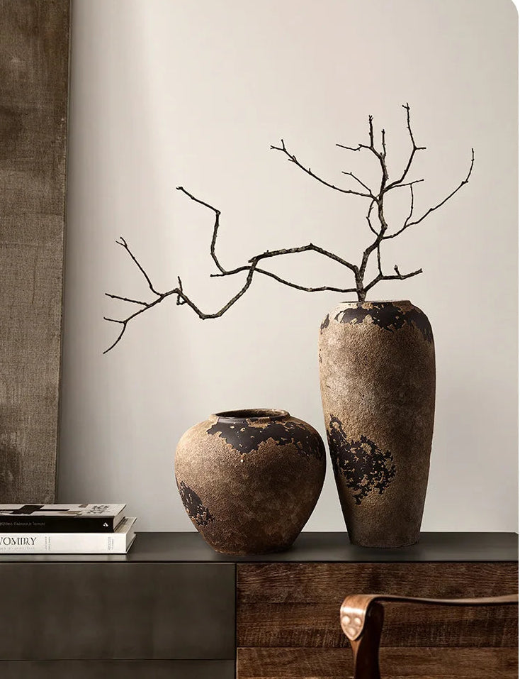Two rustic vases with branches on a wooden surface against a neutral wall.