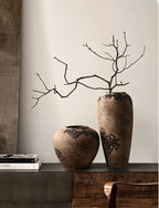 Two rustic vases with branches on a wooden surface against a neutral wall.