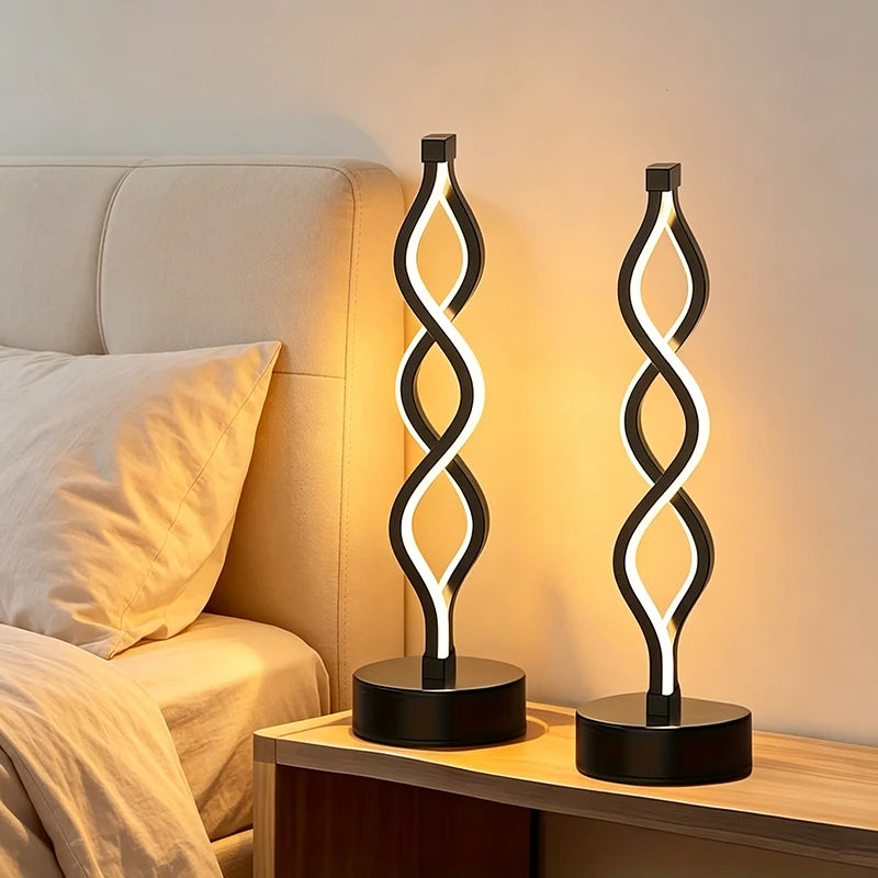 Two modern black table lamps with illuminated spiral LED designs sit on a wooden nightstand next to a bed with beige bedding.