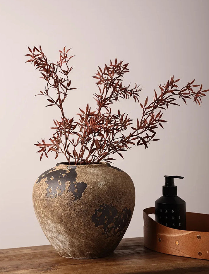 Decorative vase with dried branches on a wooden surface against a plain background