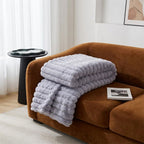 Person holding a large, fluffy gray pillow in a room with a couch and window.