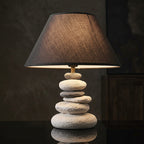 Close-up of a table lamp with a dark brown textured fabric shade and a round light beige wooden base, set against a dark brown background with the text 'NORDIC TIME, ARTIST OF LIFE.' in the lower left corner.