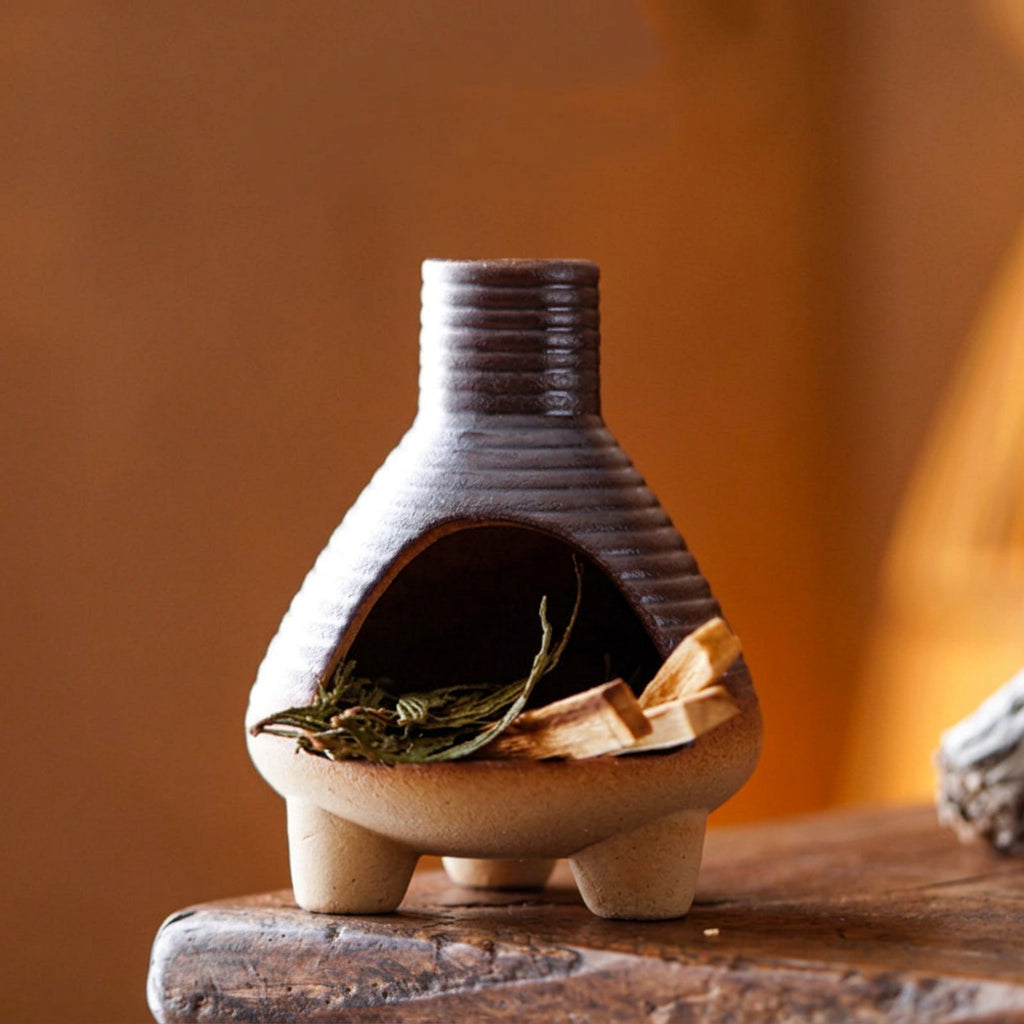 Small ceramic oven with wooden spoon and leaves on a wooden surface, against a warm brown background.