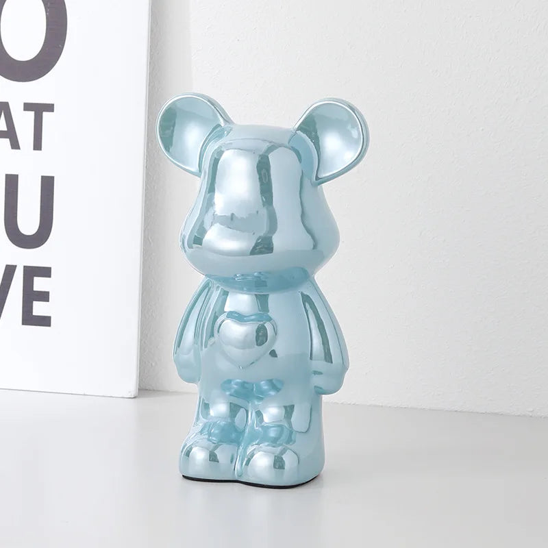 A metallic light blue bear-shaped figurine with a glossy reflective finish, standing on a white surface against a white wall with a partial decorative sign visible on the left.