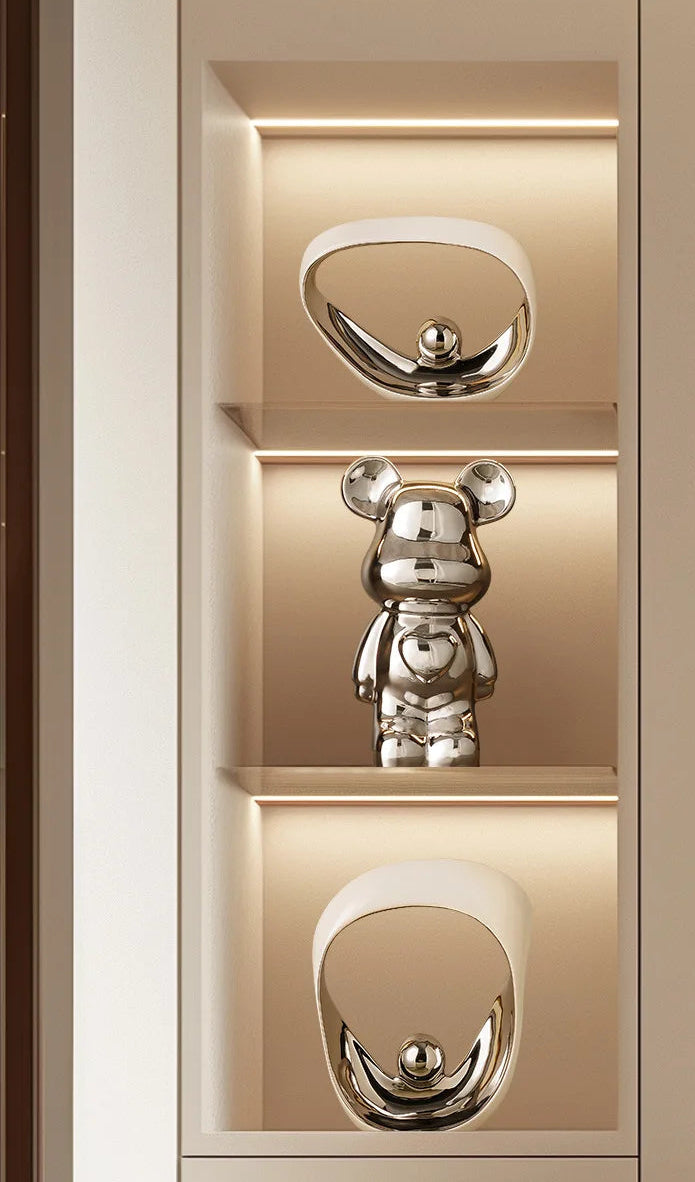 A polished silver bear-shaped figurine displayed on a lit beige shelf unit with two matching oval mirror-like pieces above and below.