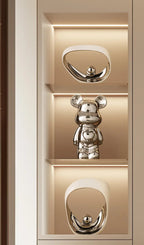 A polished silver bear-shaped figurine displayed on a lit beige shelf unit with two matching oval mirror-like pieces above and below.