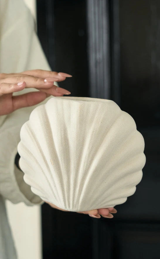 A person holds a cream-colored, shell-shaped ceramic vase or planter against a dark background. The image has a beige border with the text '# BEST WISHES FOR YOU' in the top left corner.