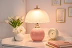 Pink ceramic table lamp with scalloped white shade on a surface.