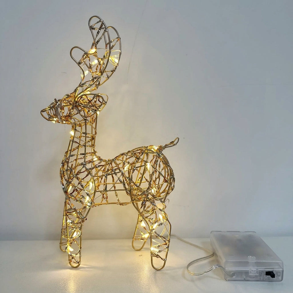 A wire-frame deer decoration with warm white LED lights, shown standing on a white surface against a light gray wall, with a small clear power adapter placed beside it.