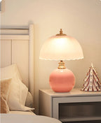 Pink table lamp on a nightstand next to a bed with a decorative item.